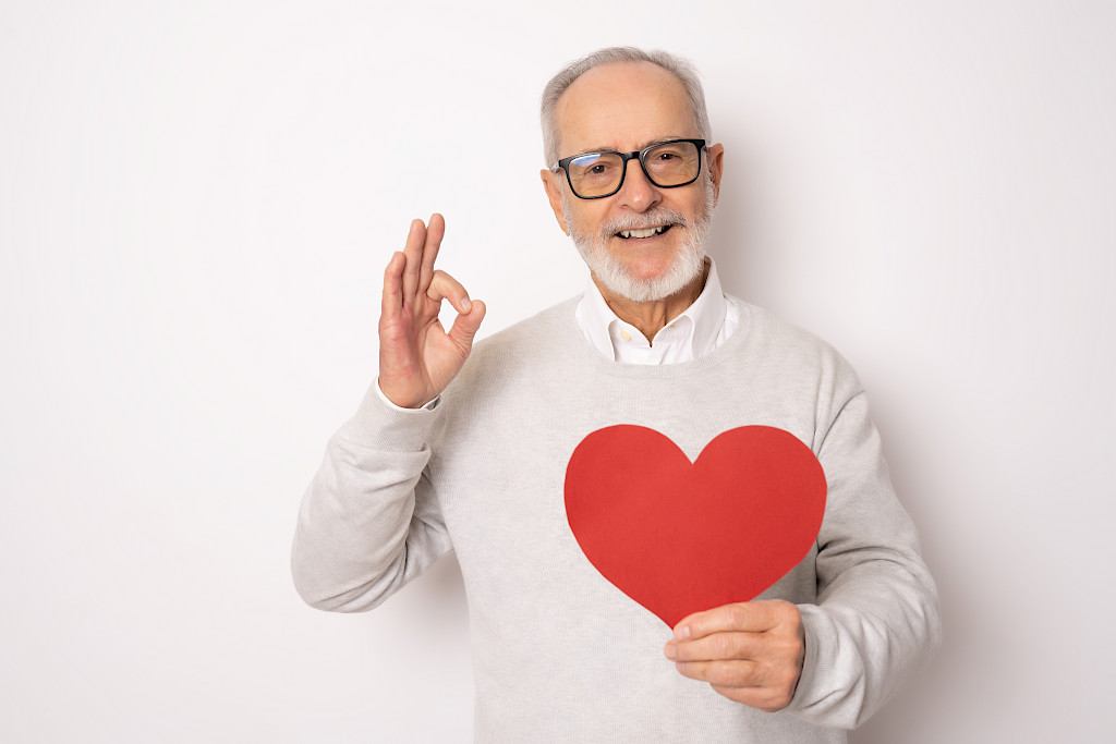 Happy senior man showing red paper heart and with okay sign isolated over white background. Health concept.